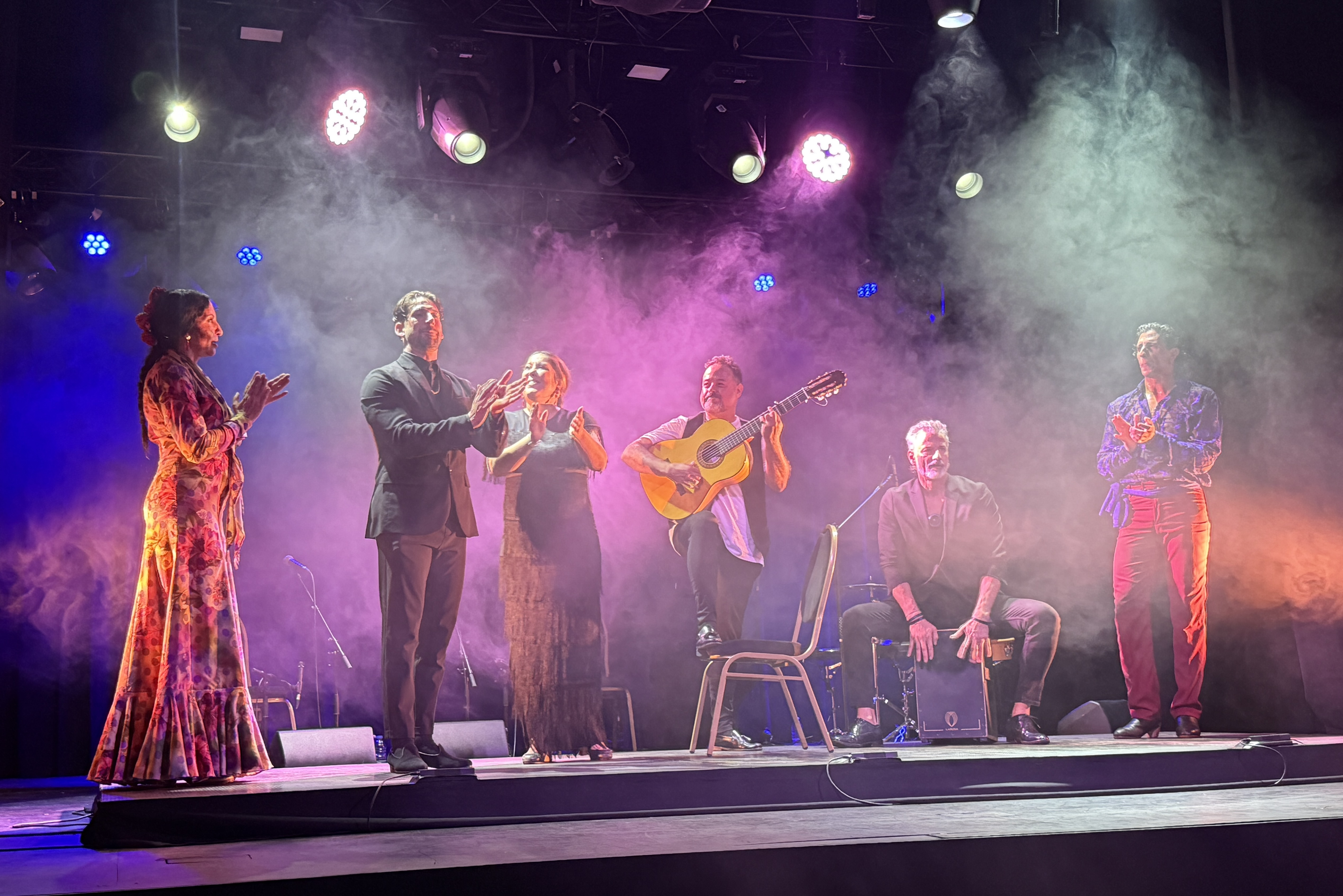 The Puerto Flamenco company clapping together under purple stage lights