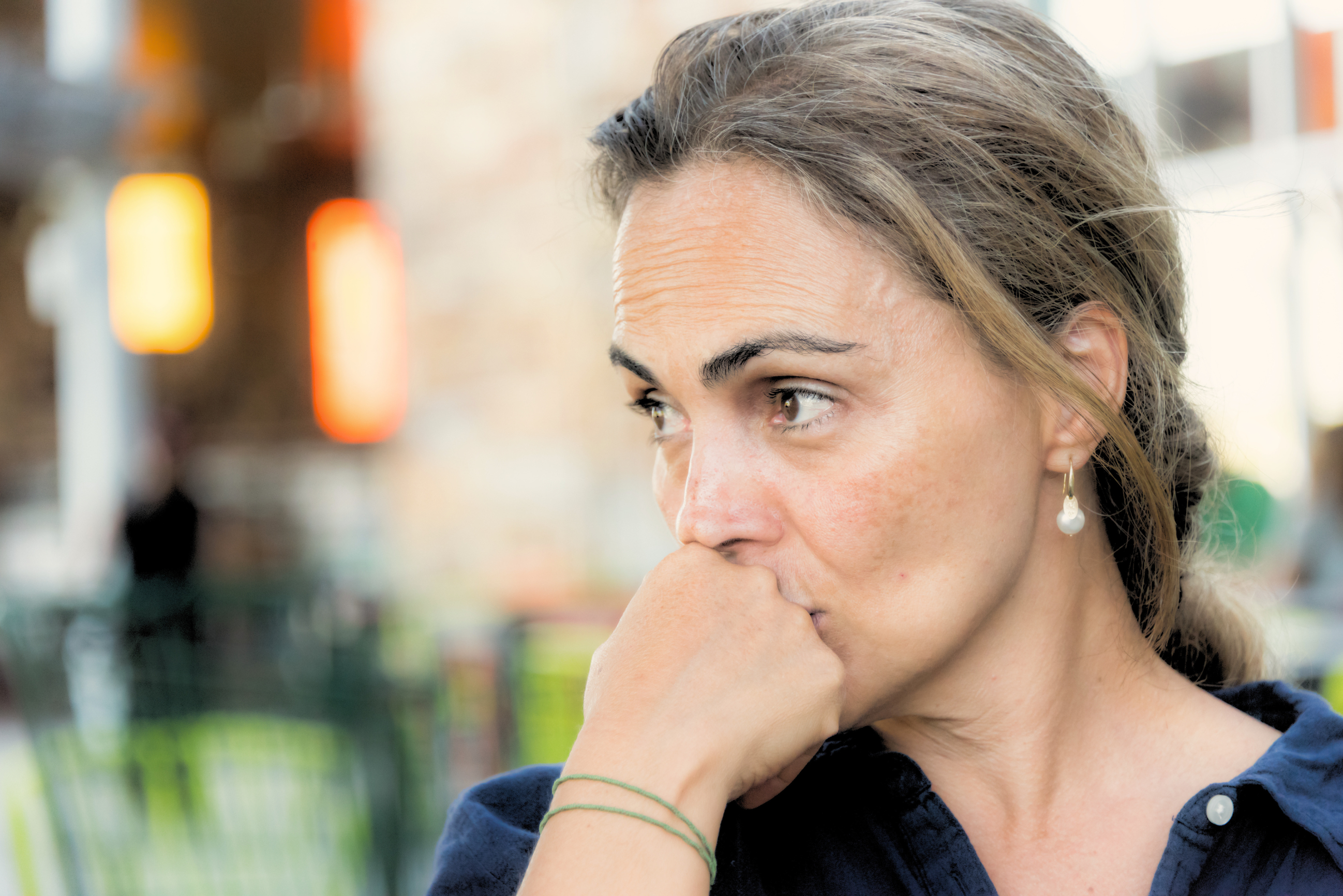 A woman in her late thirties with light brown hair, looking thoughtful with her hand near her mouth
