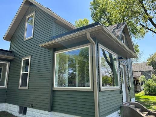 Home with dark forest green horizontal vinyl siding, white trim, large corner windows and a stone foundation