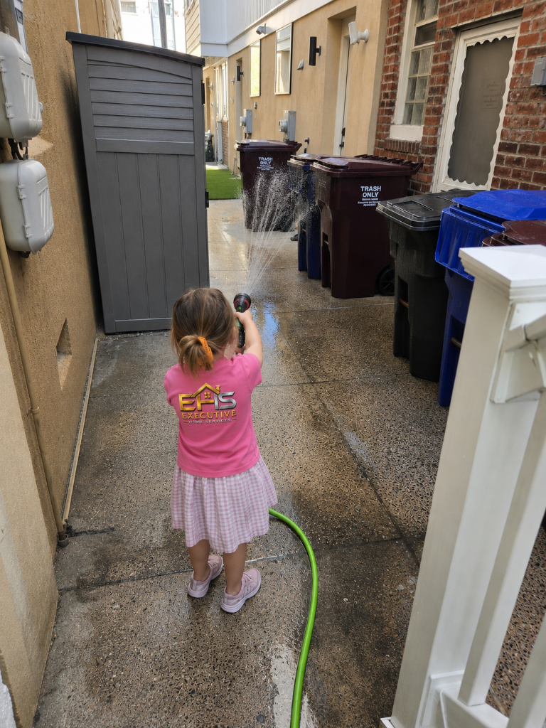 A young girl in an Executive Home Services shirt helping with the hose in a South Jersey alley