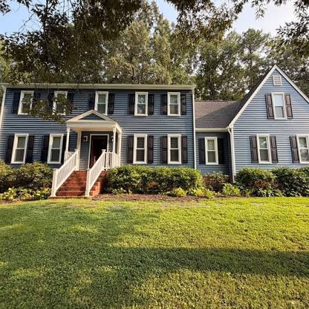 Two-story home with light blue horizontal lap siding, dark shutters, white trim and a covered portico