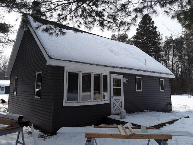 One-story gable home with dark grey horizontal lap siding, white trim, a bay window and a white entry door