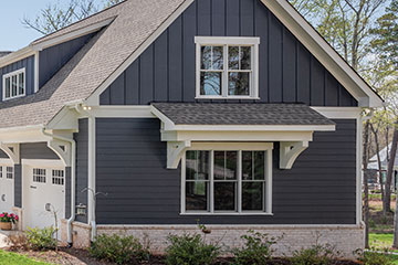 Two-story home with charcoal vertical board-and-batten siding on the upper gable and horizontal lap siding below, white trim and stone foundation