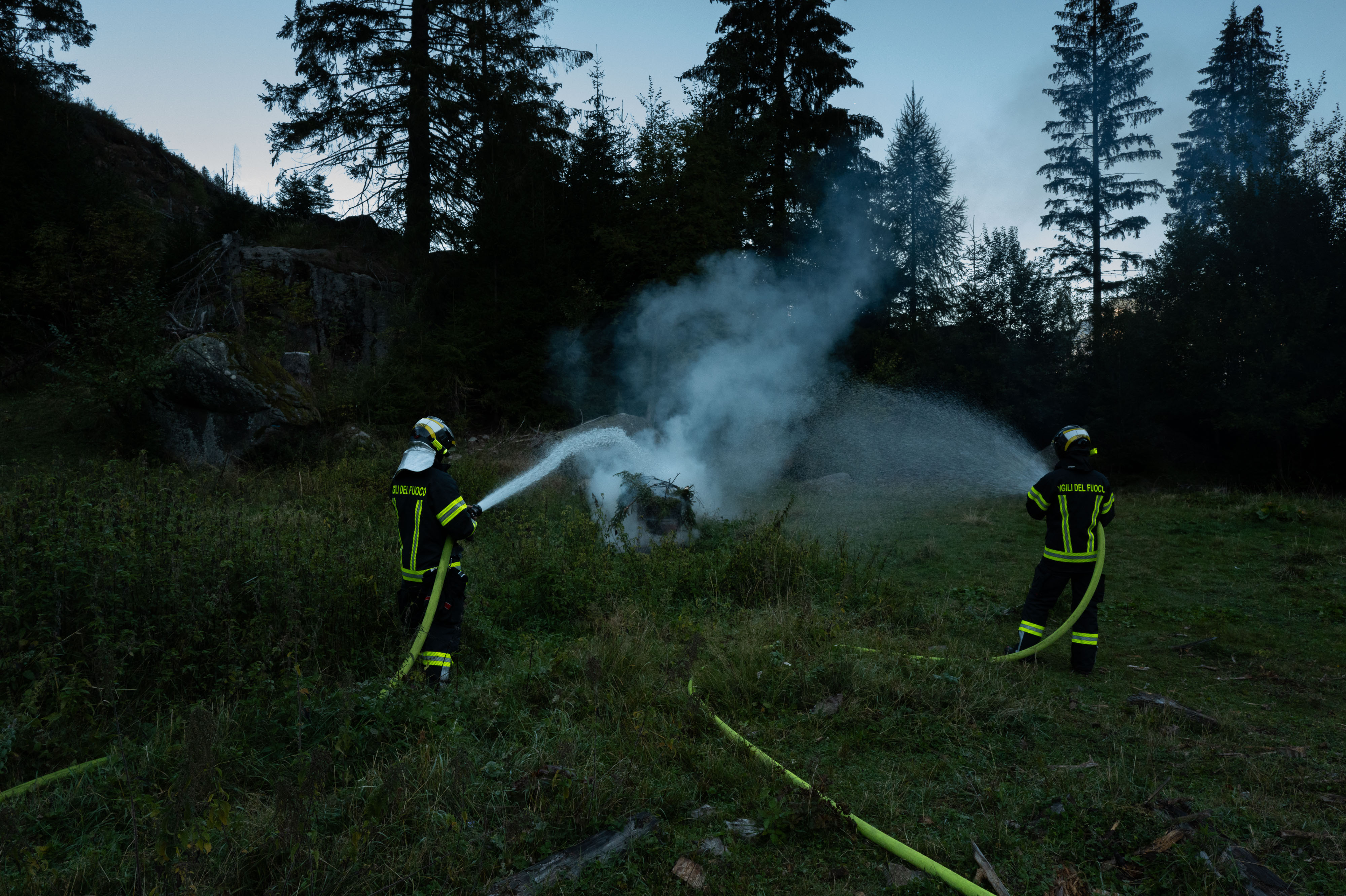 Volunteer firefighters with hoses at dusk during the wildfire simulation