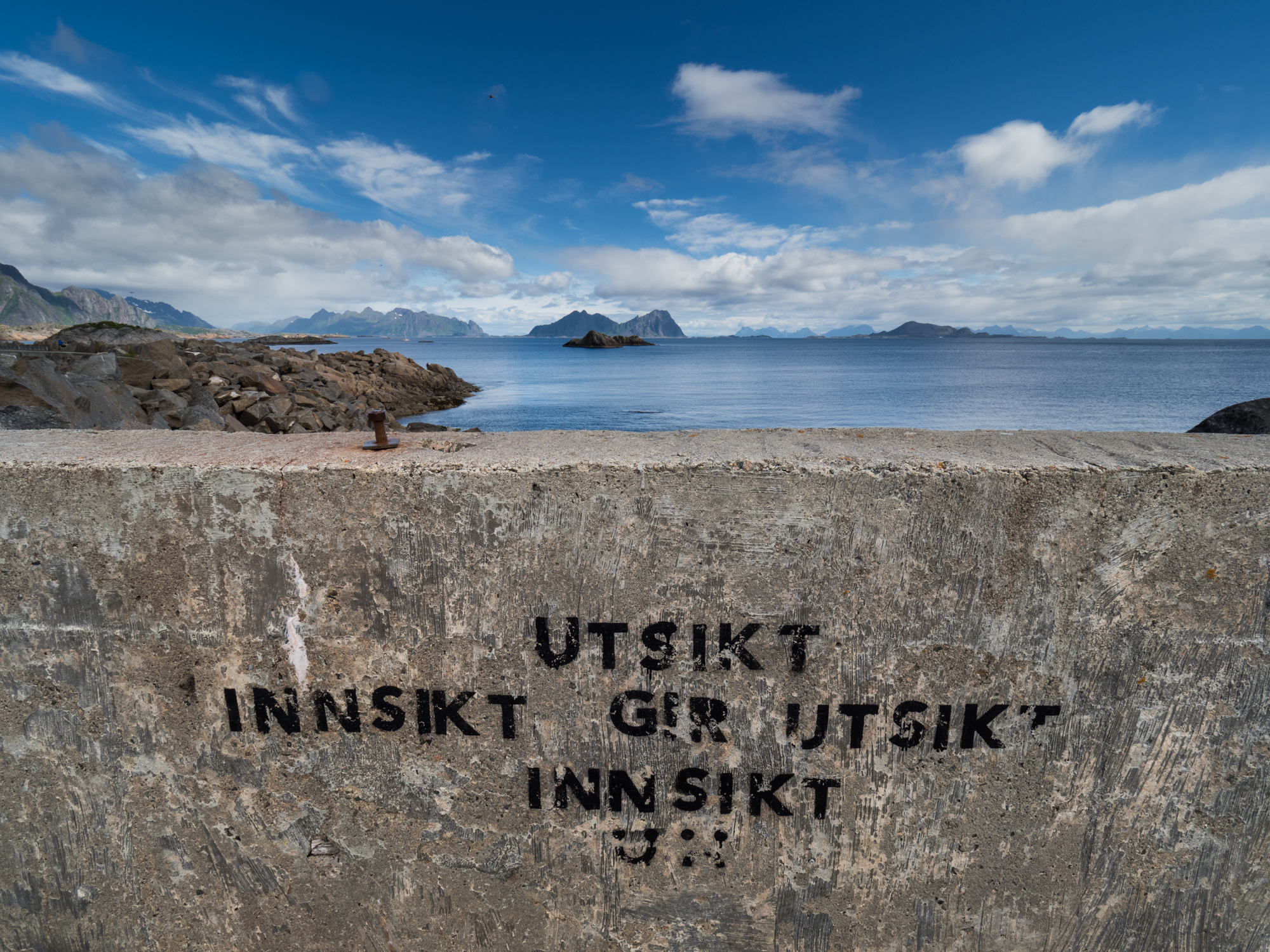 Betongmur med teksten «Innsikt gir utsikt» og utsikt mot hav og fjell
