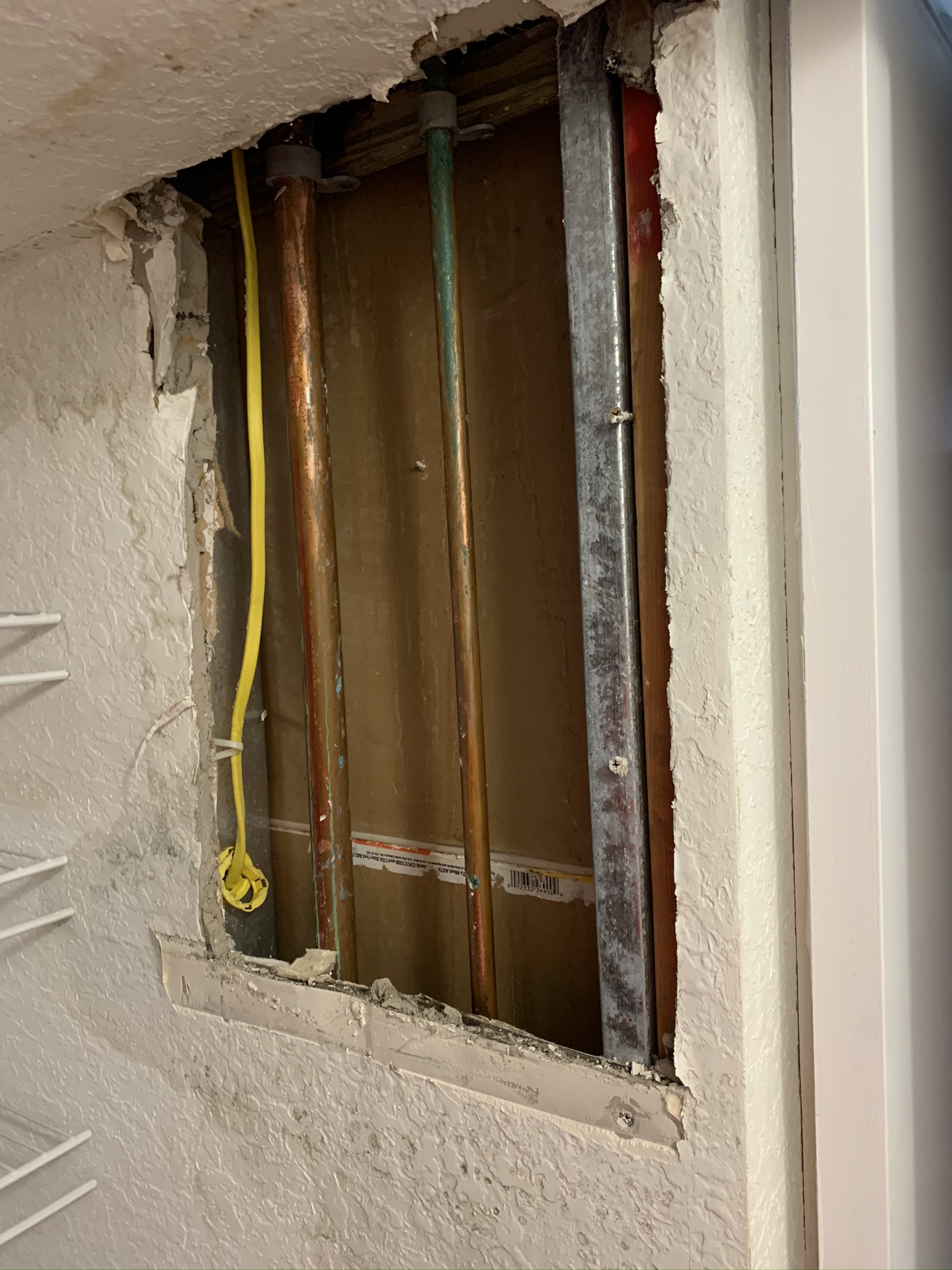Wall opened at a confirmed leak, showing the copper pipes and wiring that ran behind the drywall