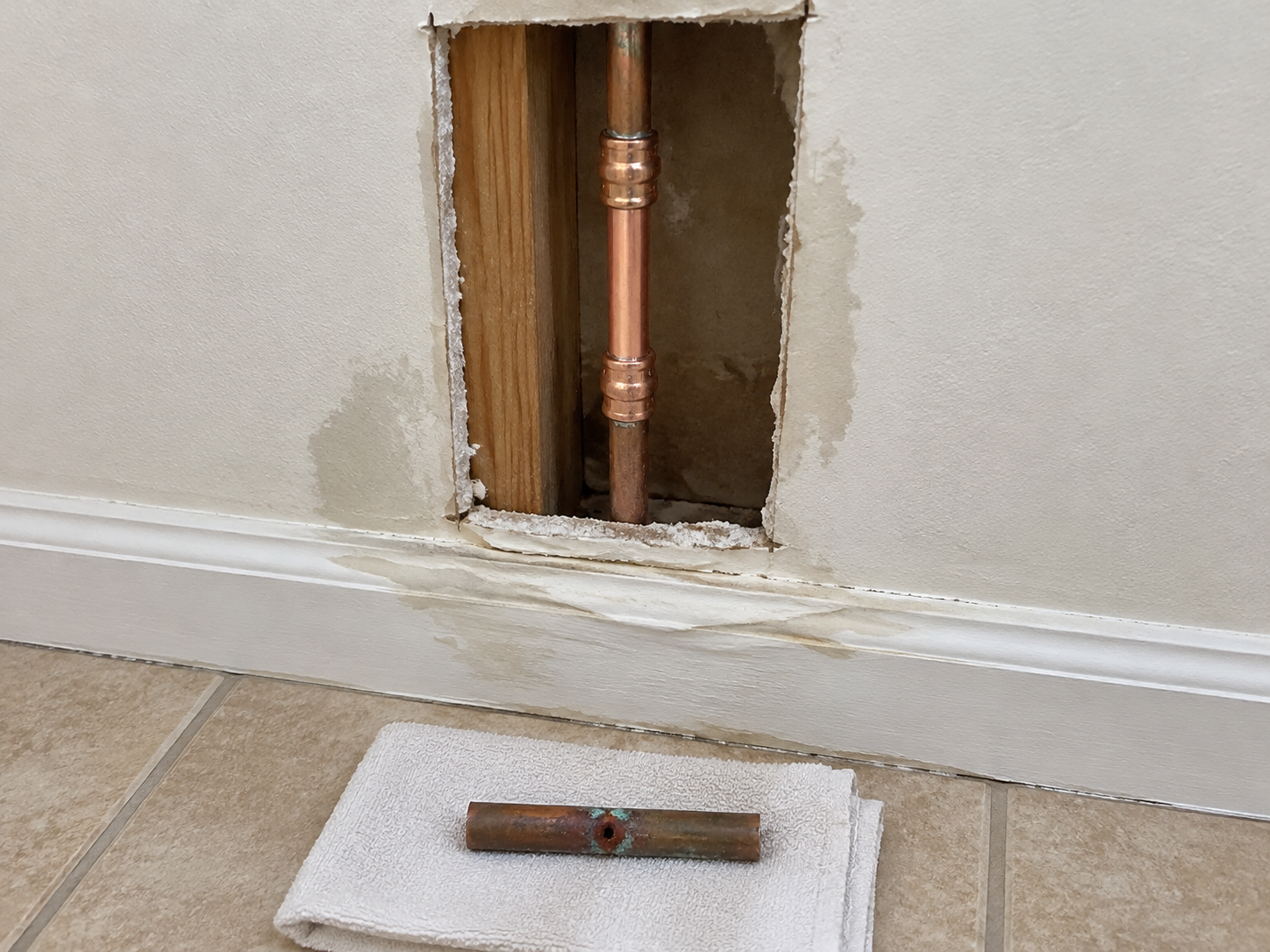 Open section of wall showing a new copper pipe repair with press couplings and the removed corroded pipe section sitting below