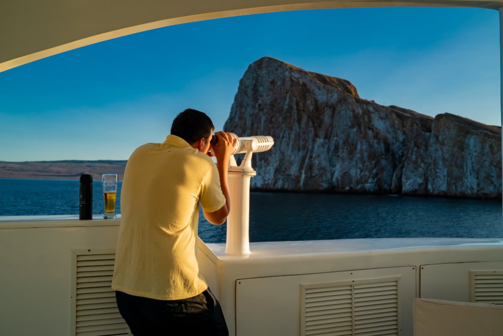 Guest with binoculars watching the Galápagos coastline by day