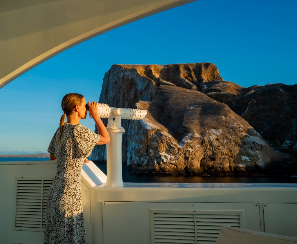 Guest using binoculars to watch Galápagos wildlife from the deck