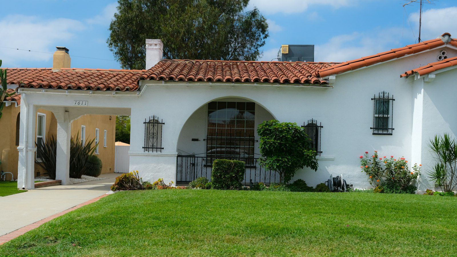 White stucco Spanish-style house with a red tile roof, an arched porch, and a green lawn
