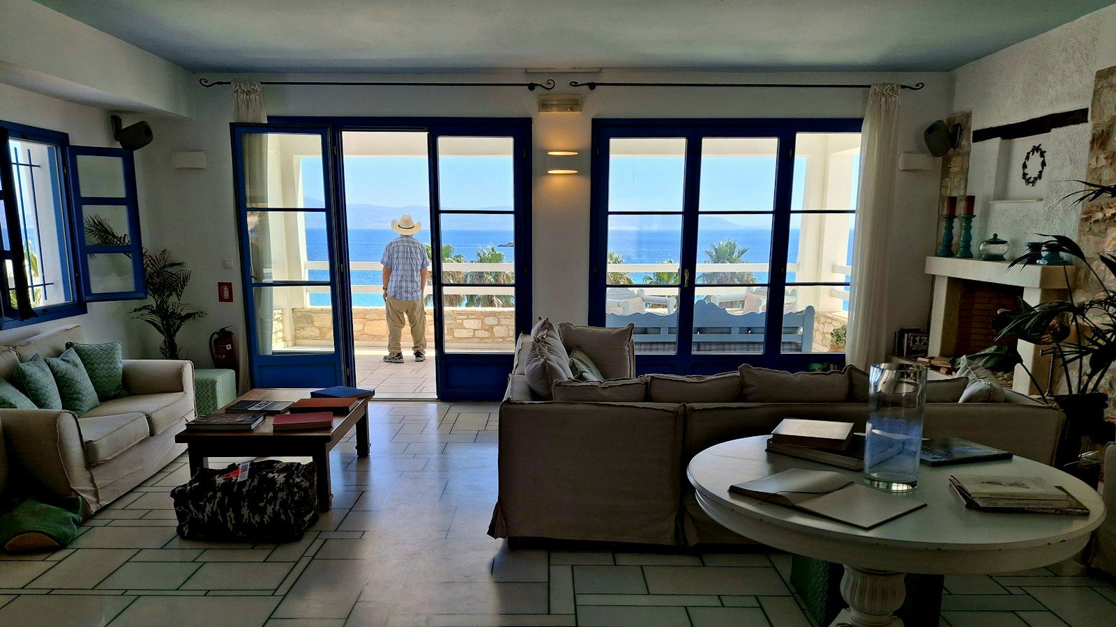 Furnished living room with gray sofas and a stone floor, glass doors open to a balcony overlooking the sea