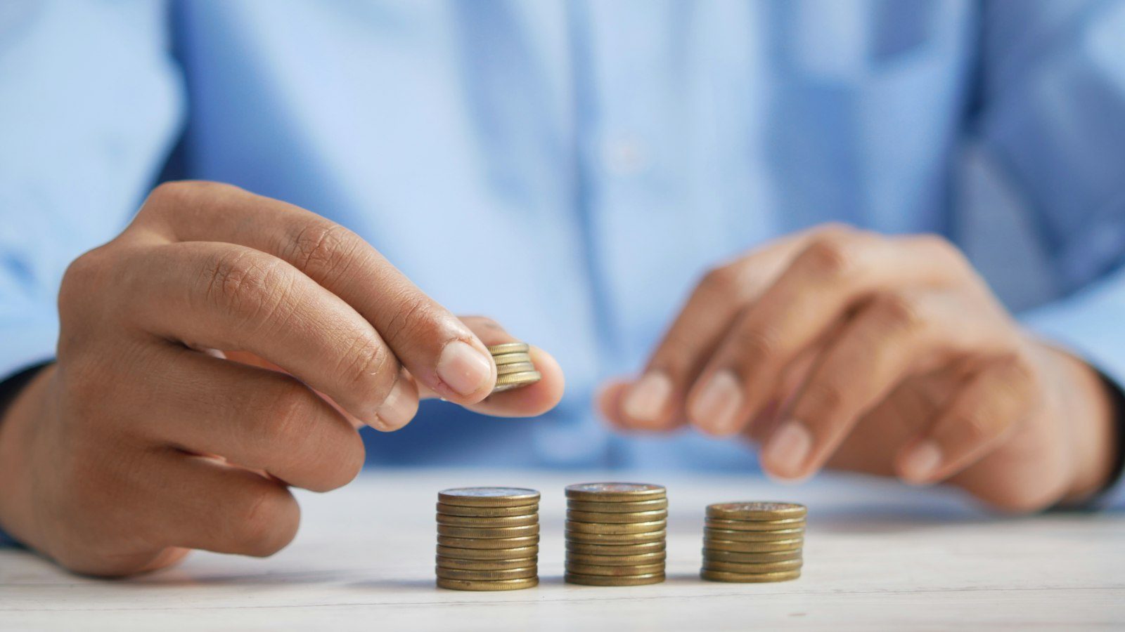 Man in a light-blue shirt placing a coin on one of three short stacks of coins