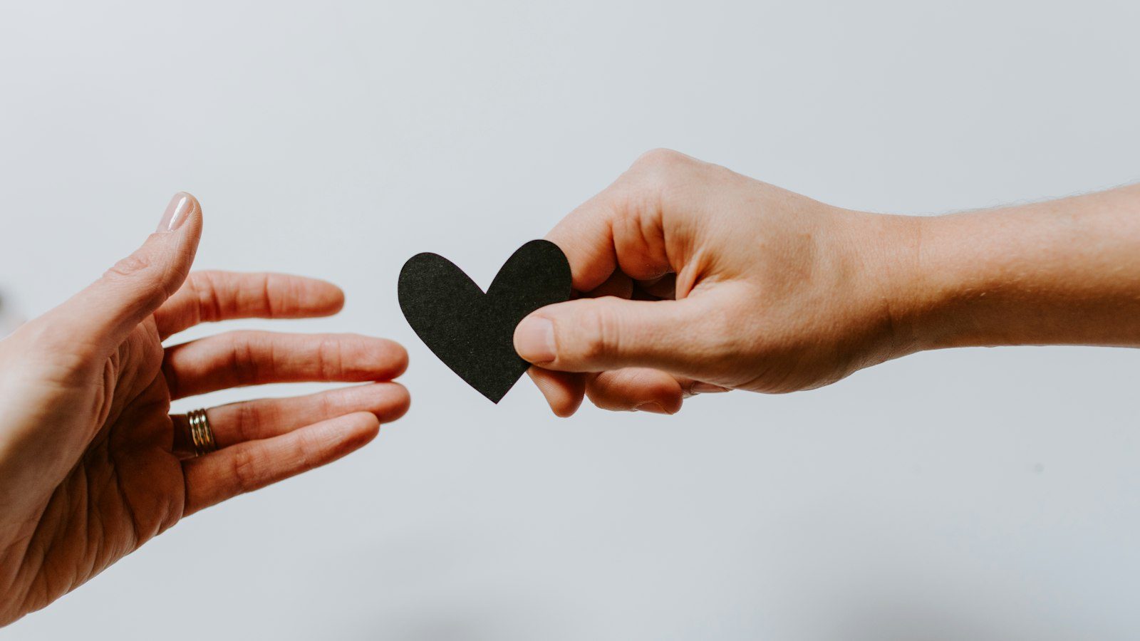 One hand offering a black paper heart to another open hand