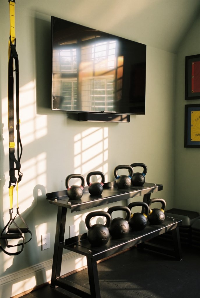 Wide-angle view of the Oak & Iron home gym showing treadmill, stationary bike, weight bench and arched window with plantation shutters