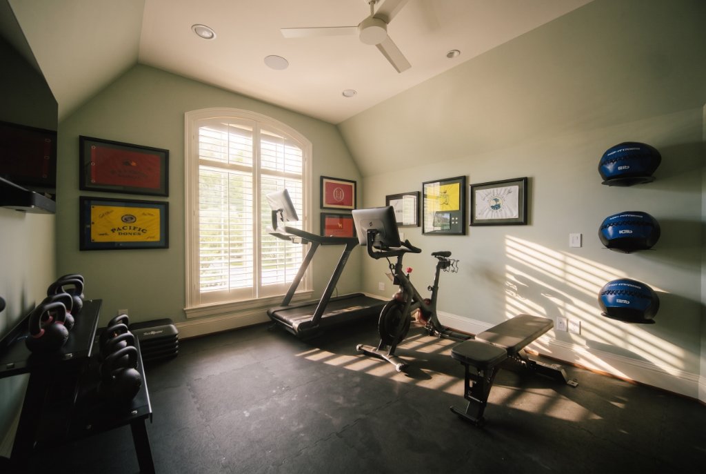 Bright second-floor home gym in Preston Hollow with treadmill, exercise bike, weight bench, kettlebell rack and sage green walls