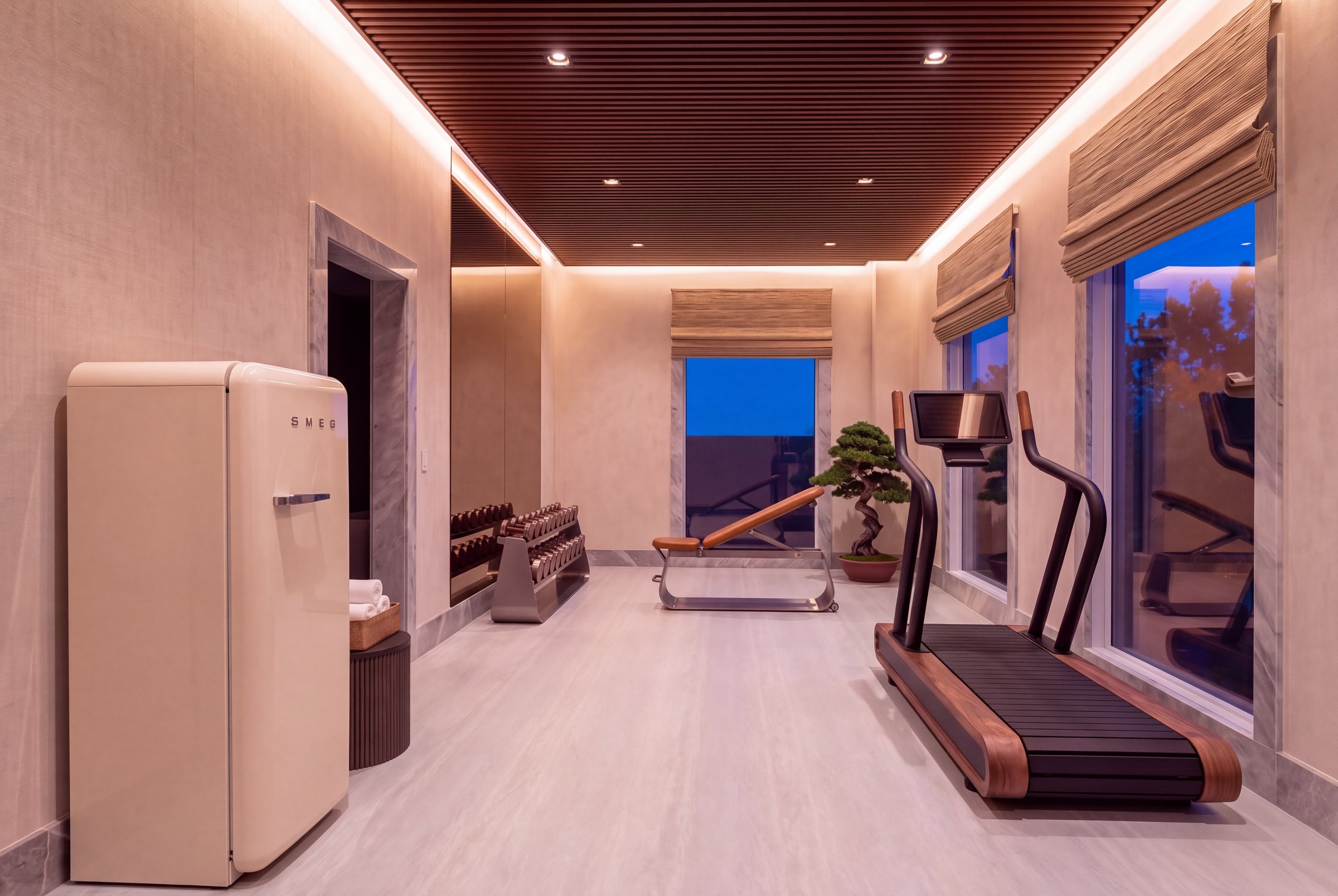 Rendering of Tanren at Kips Bay Decorator Show House Dallas 2026 showing a cream Smeg refrigerator, walnut and stainless dumbbell rack, adjustable bench, walnut NOHrD treadmill, Perennials Tableau wallcovering in Chalk, Marble Silver PaviFlex floor and a floating walnut slat ceiling