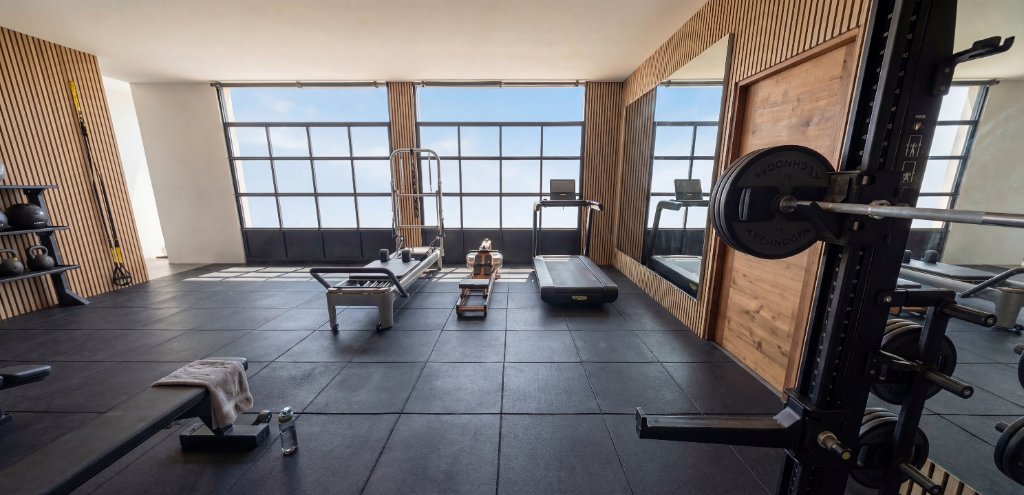 Render of West Texas Sweat gym showing cardio equipment, dumbbell rack, stability balls and warm walnut wood slat walls
