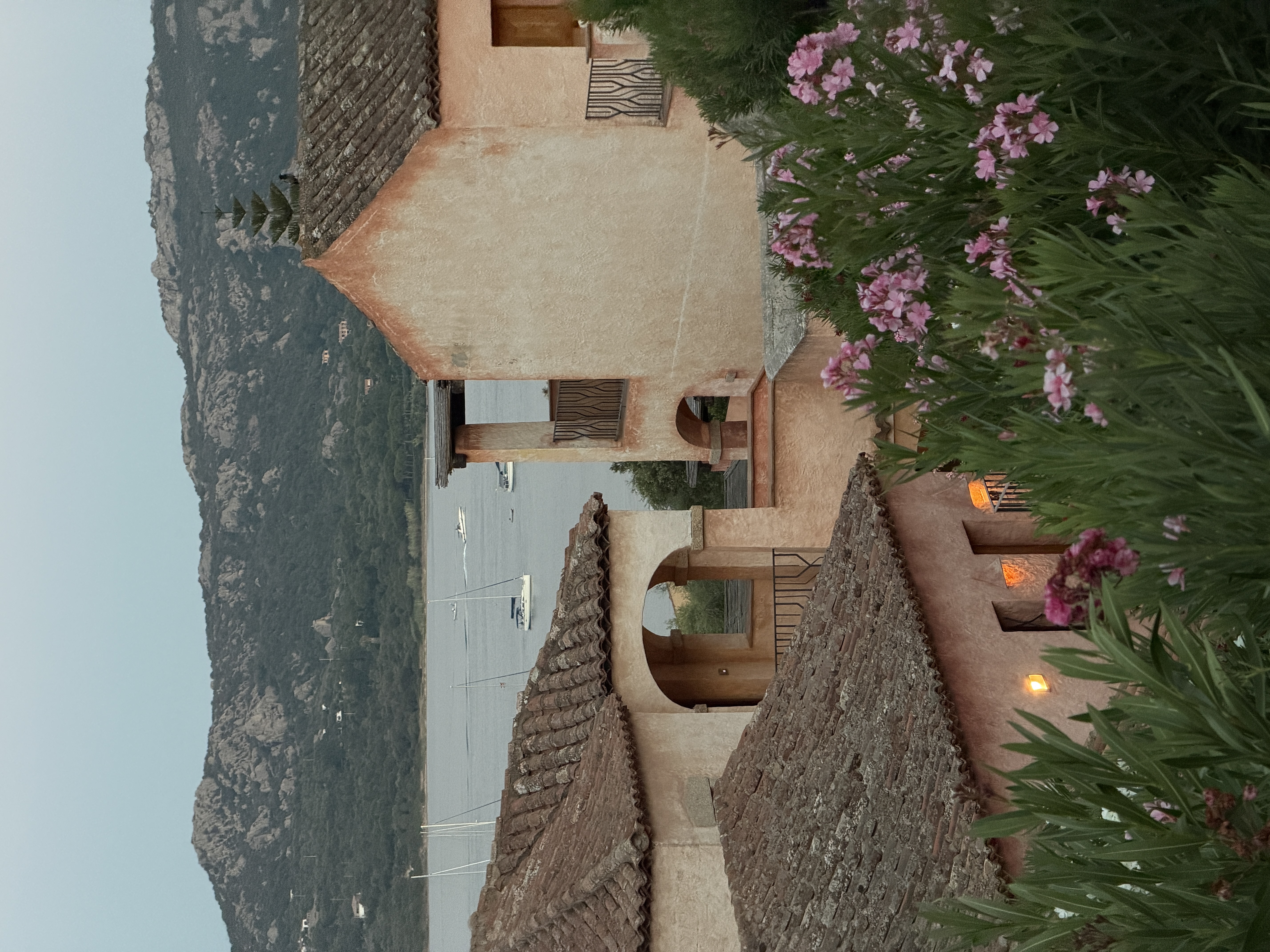 Terracotta stucco buildings with arched entryways at dusk, pink oleander in foreground