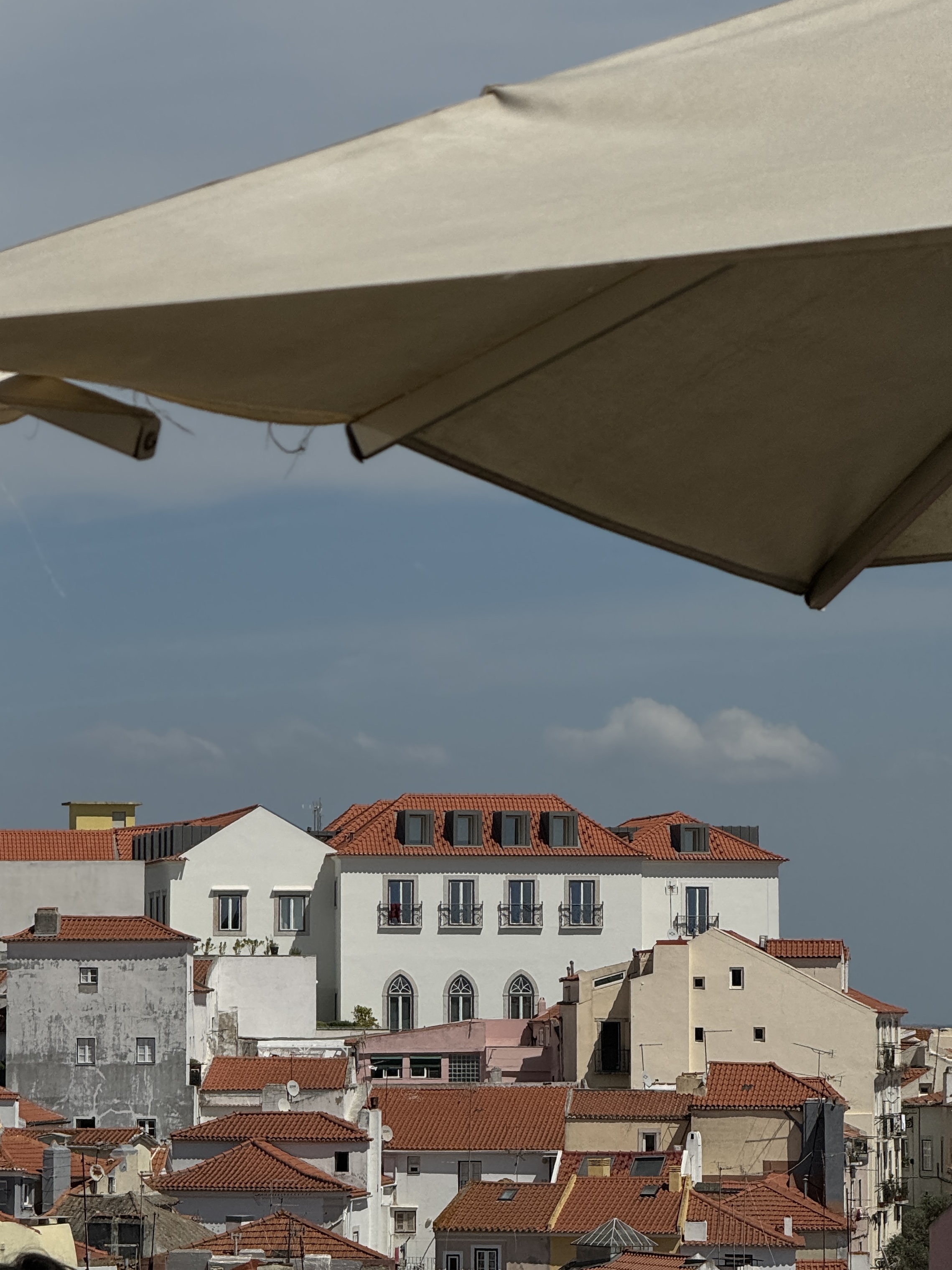 Lisbon-style terracotta rooftops with dormer windows, seen under a pale parasol