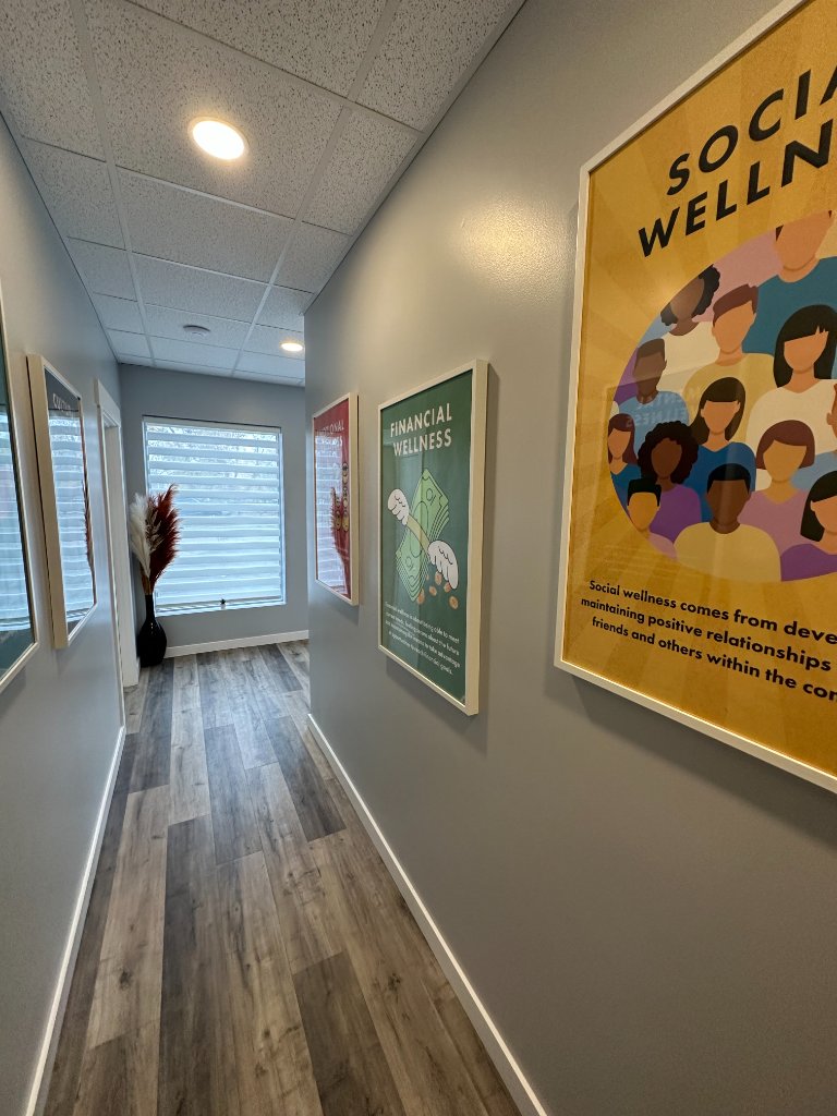 Bright clinic corridor displaying framed Wellness Dimensions educational posters at Mind360 St. Albert.