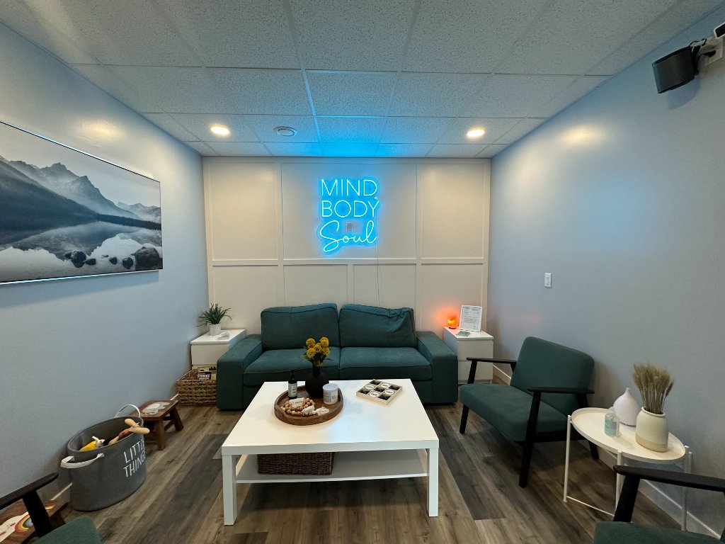 Comfortable client waiting area at Mind360 St. Albert featuring a teal sofa and a neon Mind Body Soul sign.