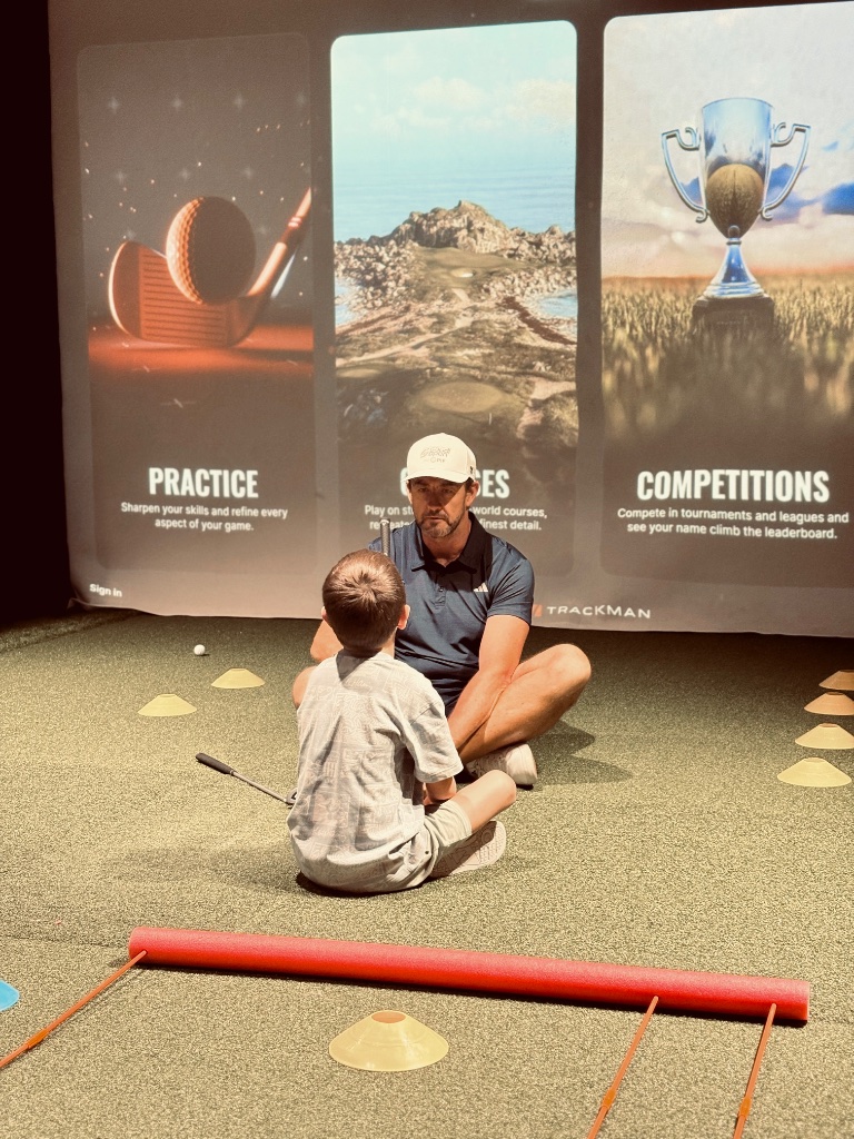 Junior golfer and coach reviewing practice, courses, and competitions on a Trackman simulator screen