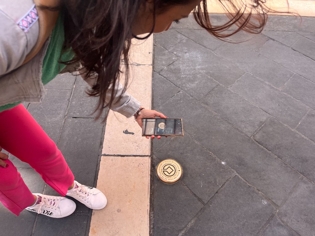 Mains tenant un smartphone au-dessus d'un repère en laiton incrusté dans le sol à Nice