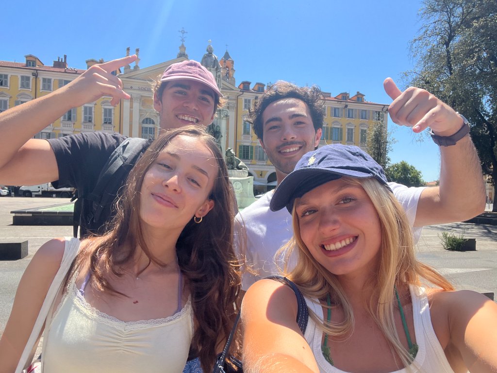 Quatre amis posant pour un selfie groupé sur une place ensoleillée de Nice