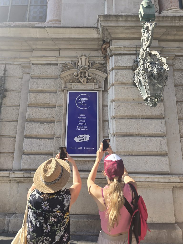 Deux personnes photographiant l'enseigne de l'Opéra Nice Côte d'Azur sur un mur en pierre