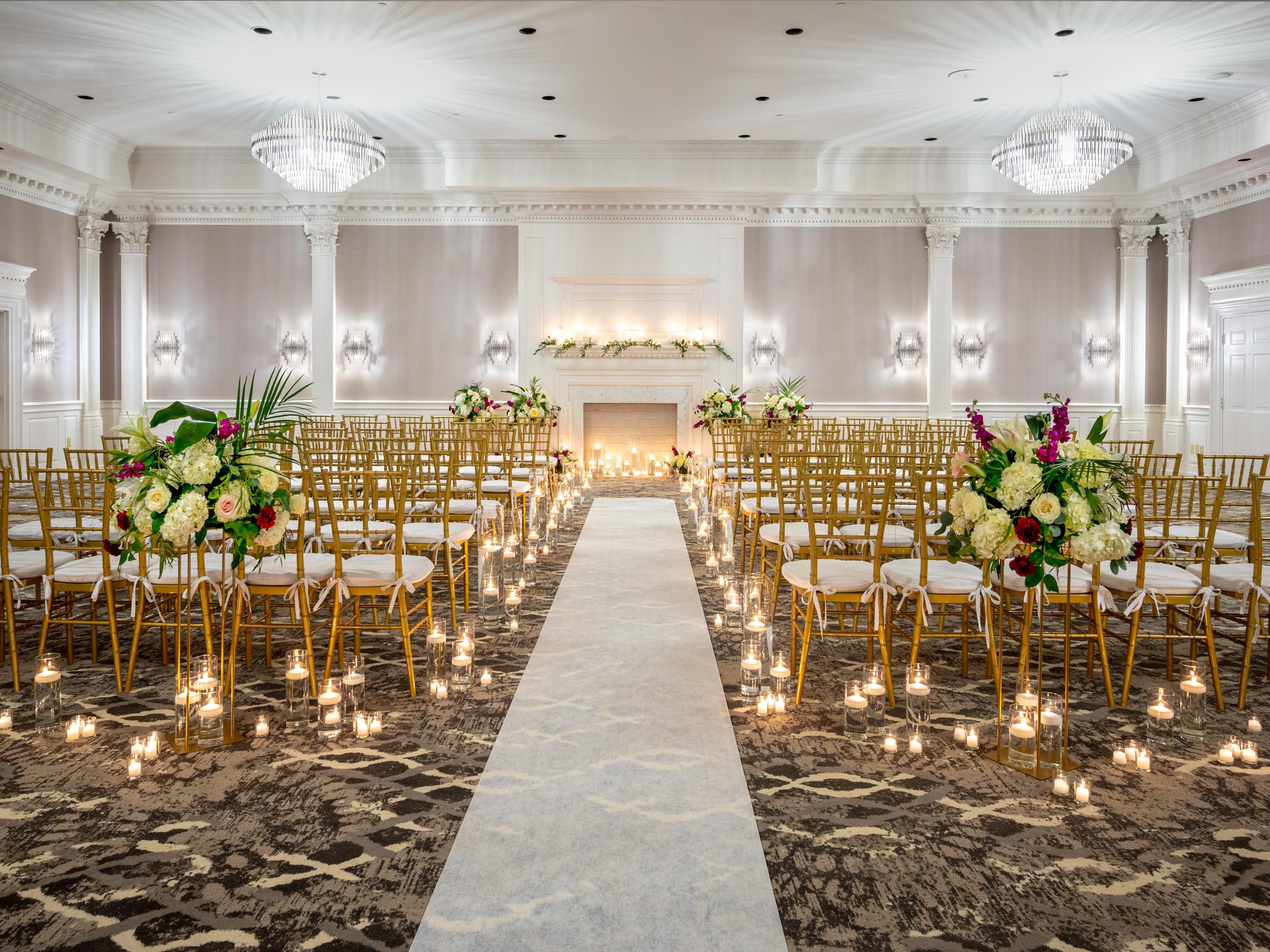 Formal ceremony hall with candle-lined aisle and gold chairs