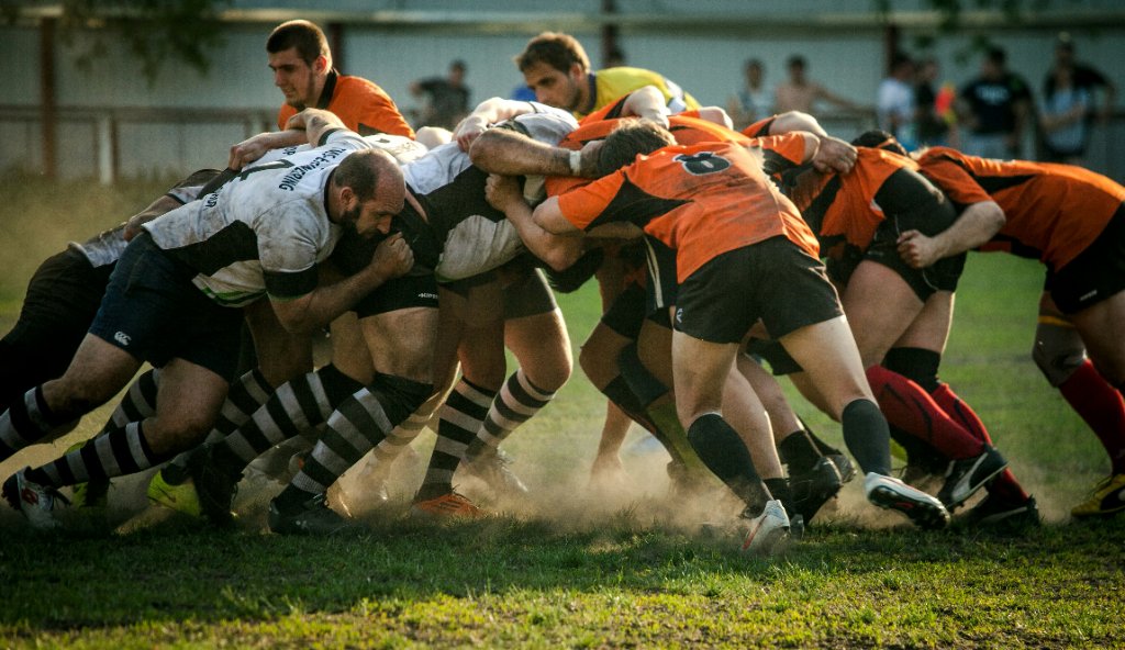 A rugby scrum in progress, players locked together under floodlights