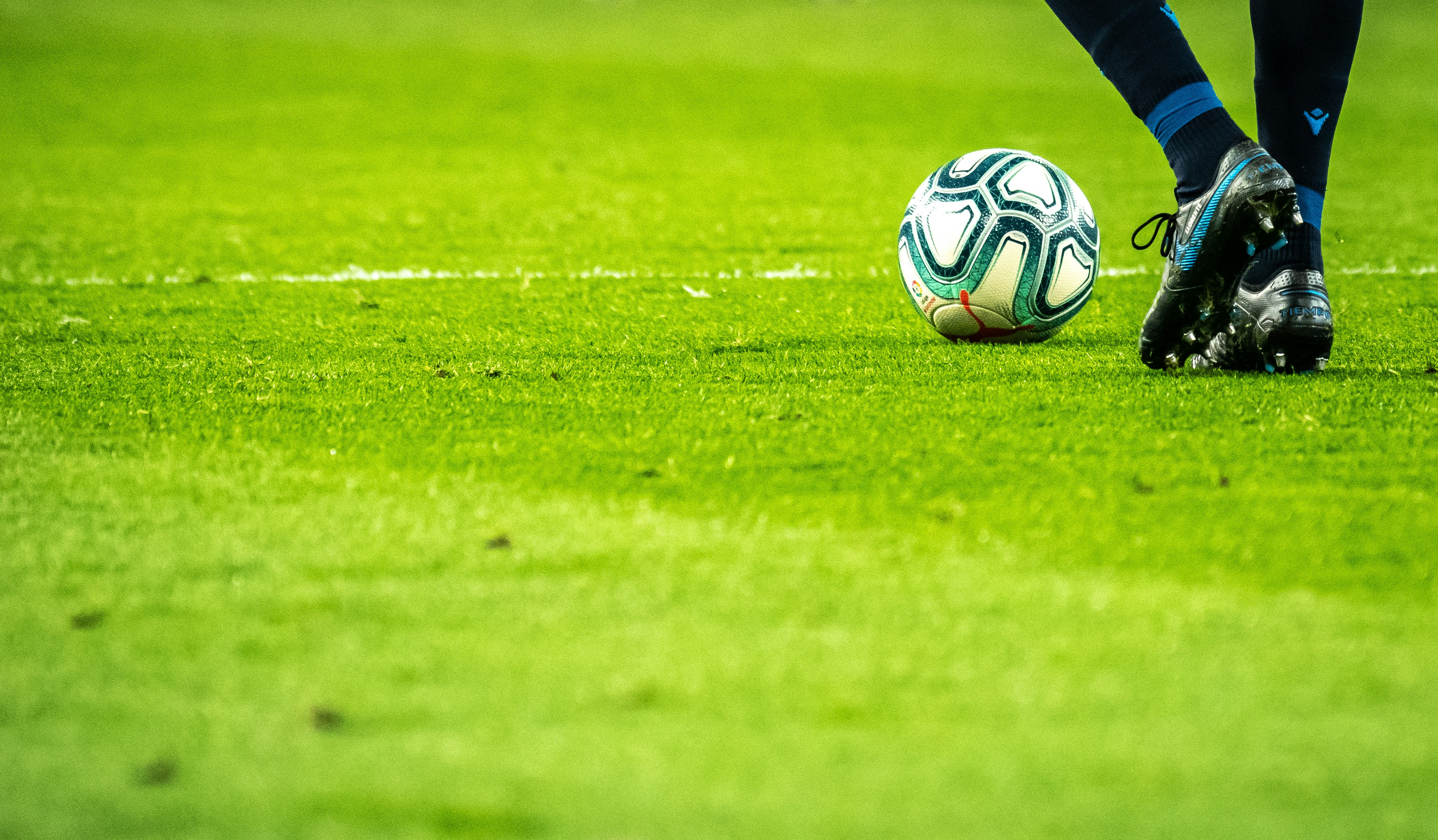A football resting on a vibrant green pitch beside a player's boots