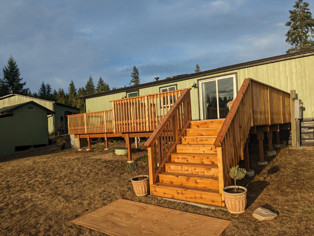 Raised wood deck with staircase and vertical baluster railing attached to a manufactured home.