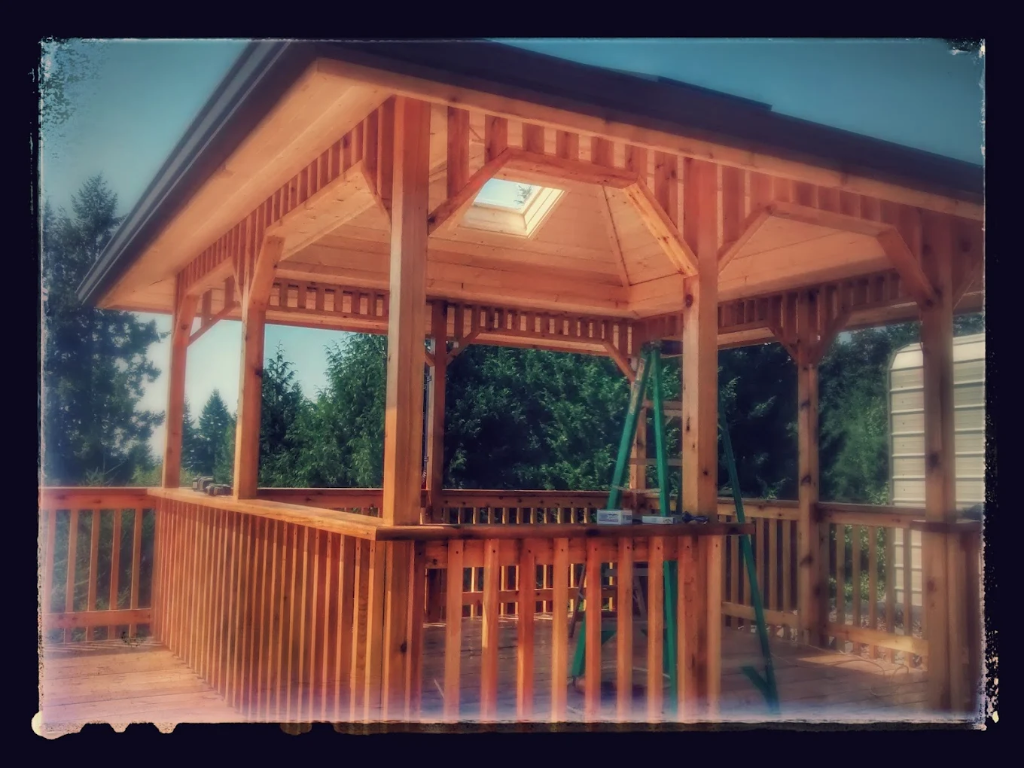 Wood gazebo with octagonal roof, central skylight, exposed beam framing, and spindle railing on attached deck.
