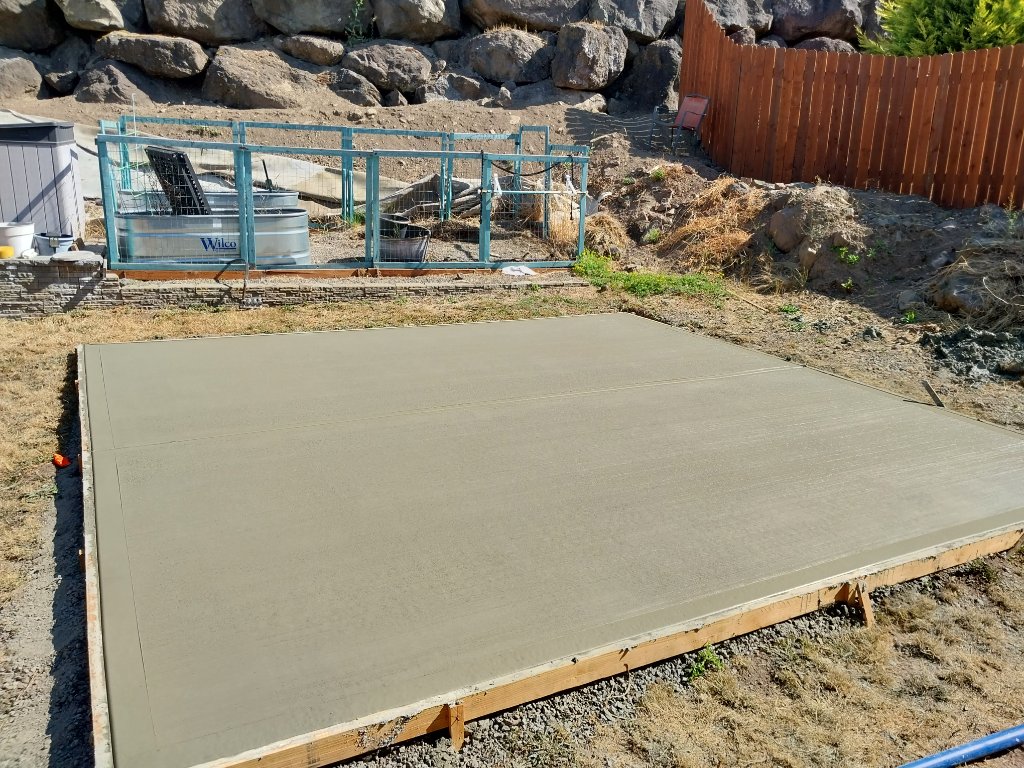 Freshly poured and broomed concrete slab with control joints and wood form boards still in place.