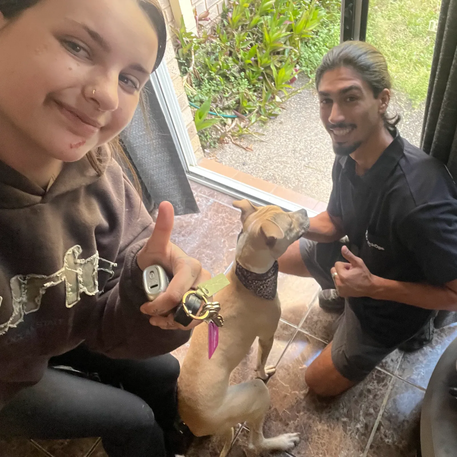 Customer holding her keys with a thumbs up, her dog and the LockOps technician beside her