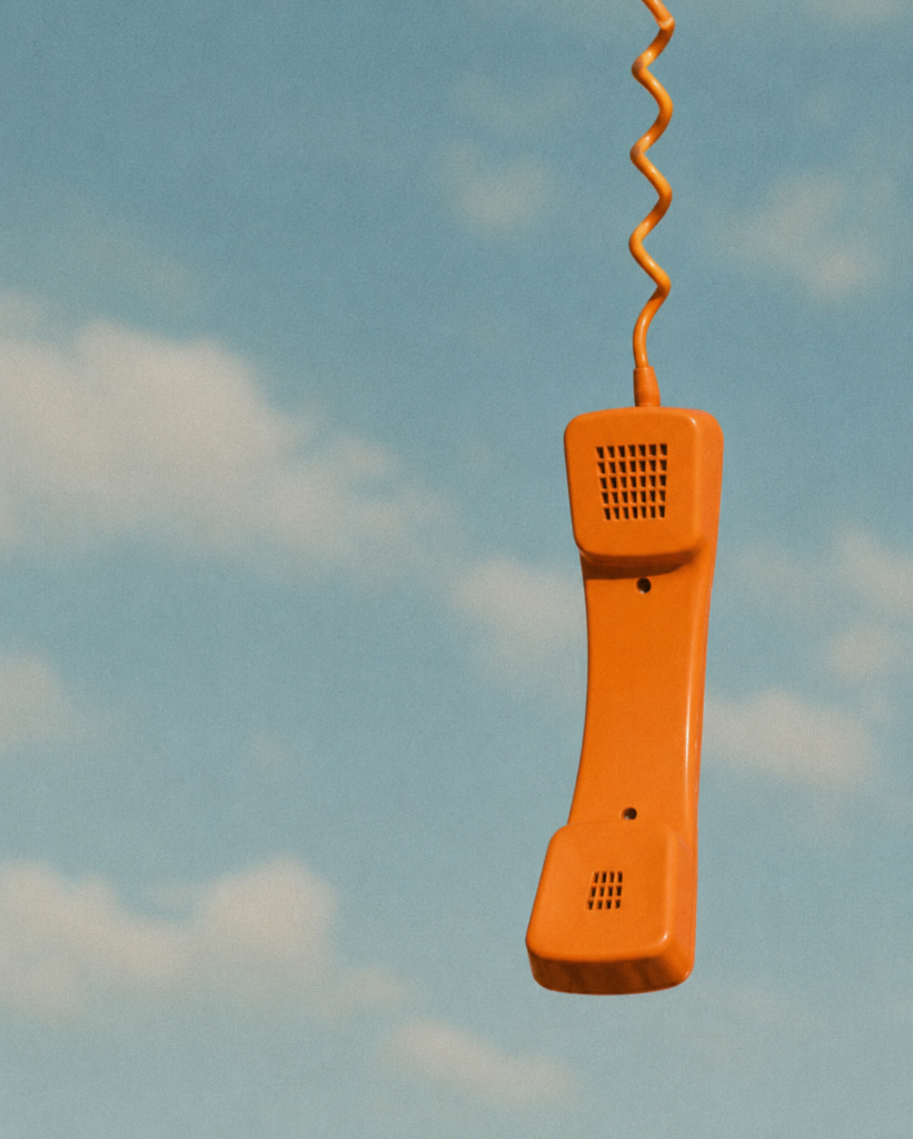 An orange retro telephone handset suspended against a light blue sky
