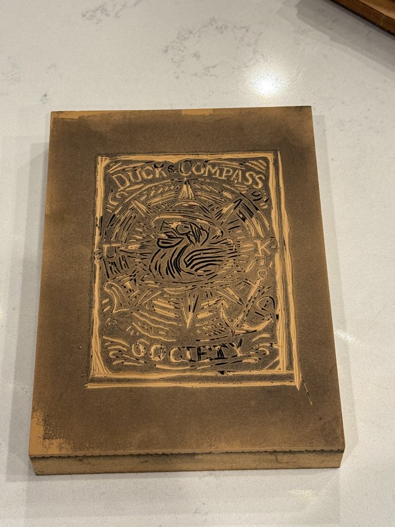 Hand-carved woodblock stamp of the Duck & Compass Society logo