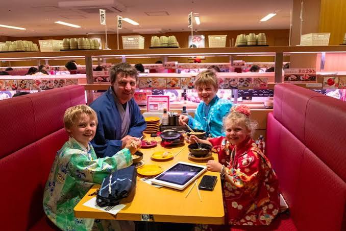 A family of four in kimonos dining at a conveyor-belt sushi restaurant with red vinyl booth seating