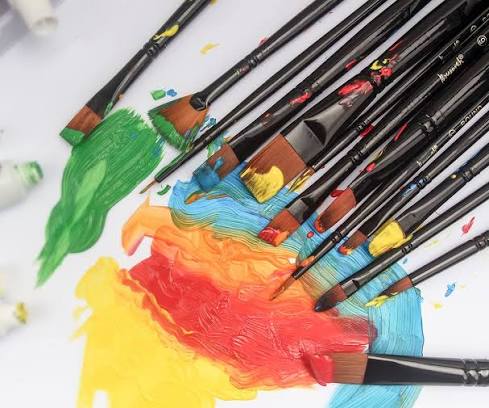 Paintbrushes fanned across colorful watercolor paint swatches on a white studio surface