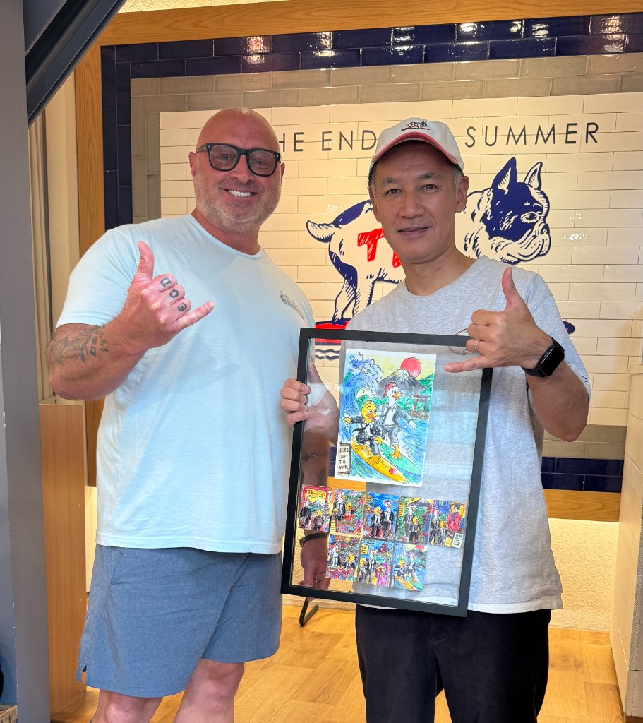 Two men holding a framed Duck & Compass Society card collection, making shaka signs