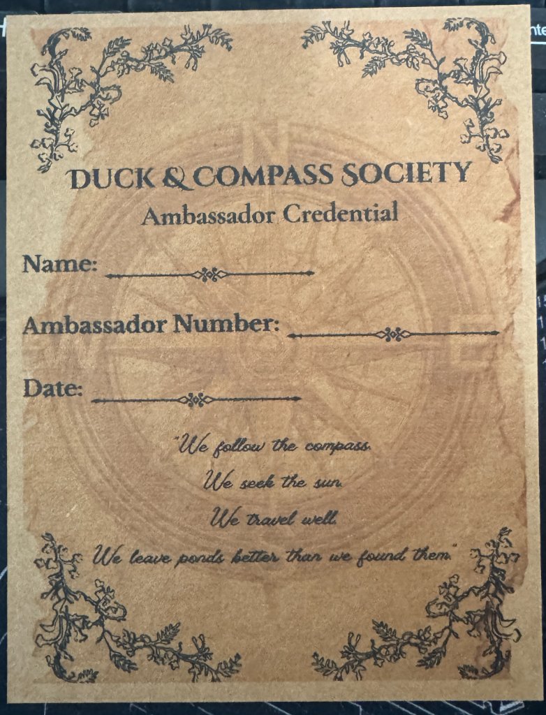 Ambassador Credential card for the Duck & Compass Society on textured parchment paper with compass rose and ornate border