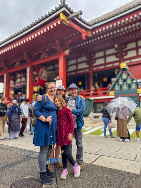 A family of four posing outdoors in front of a traditional Japanese temple with deep red wooden pillars