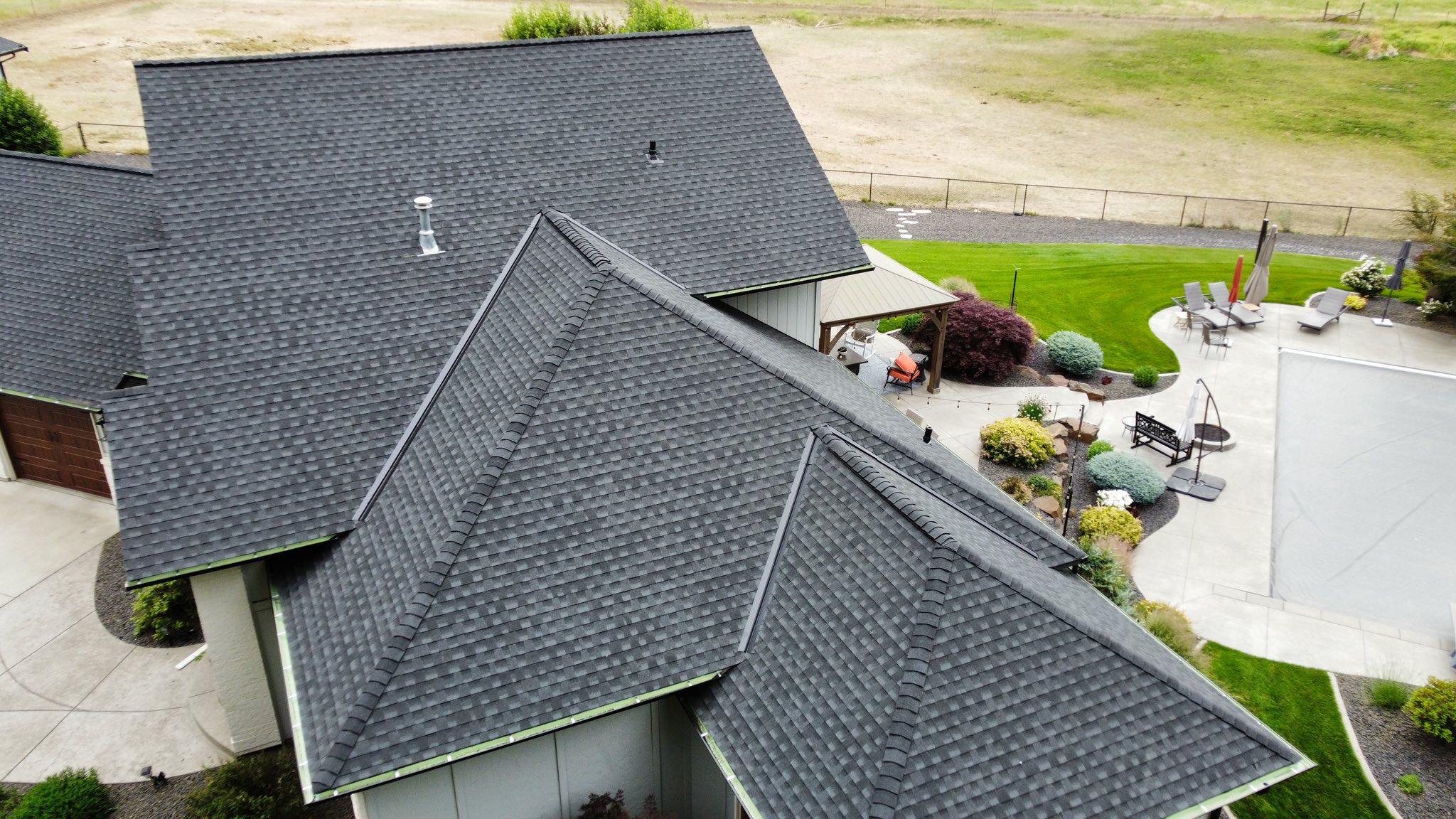 Aerial drone view of a residential home with a complex multi-gabled dark grey architectural shingle roof