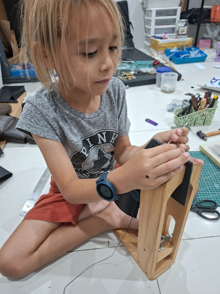 A child hand-stitching leather at a stitching pony