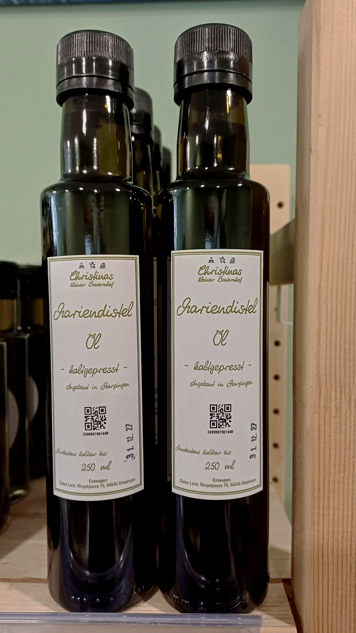 Zwei Flaschen kaltgepresstes Mariendistelöl von Christinas kleinem Bauernhof auf einem Holzregal