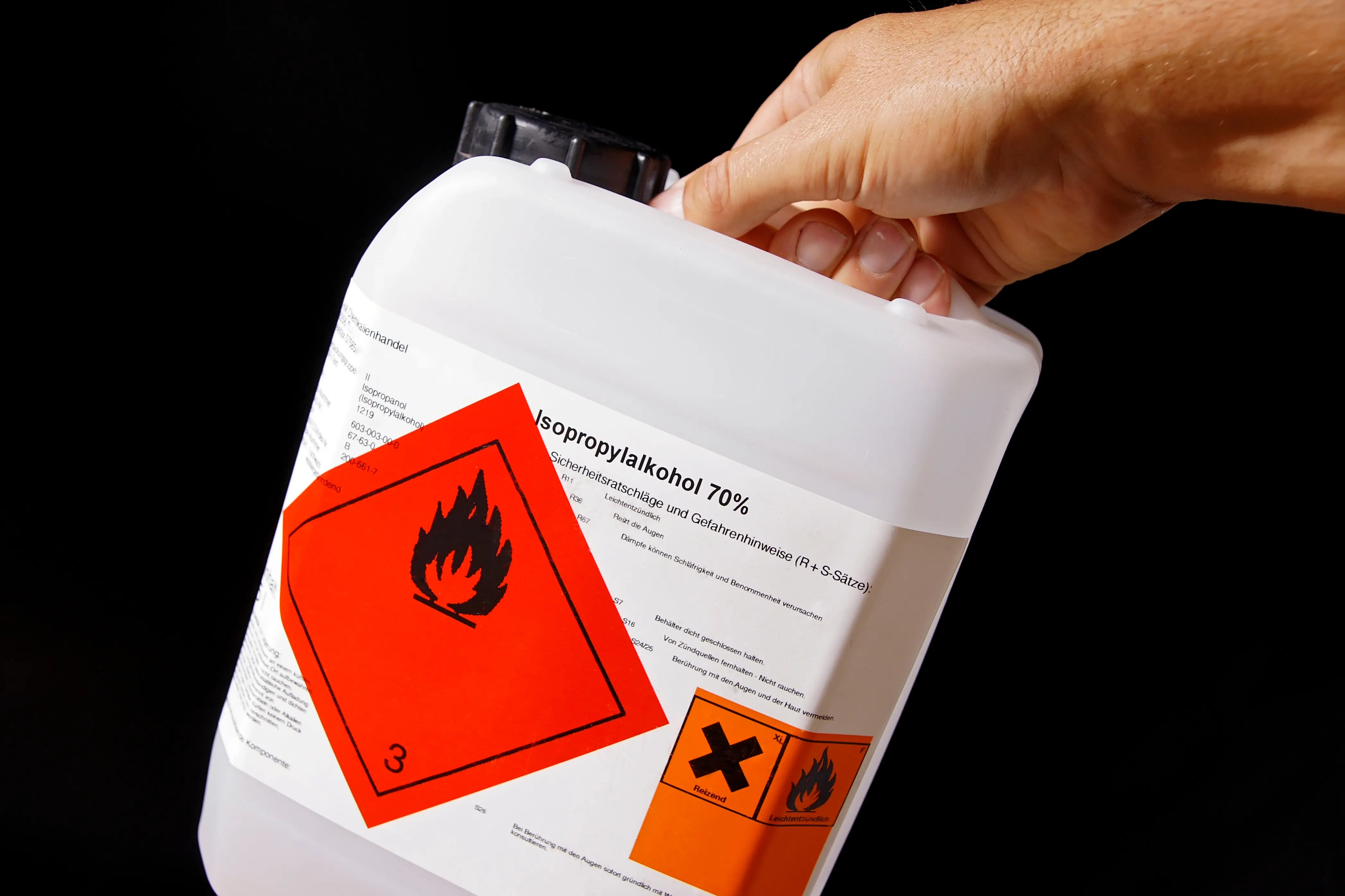 Hand hält Kanister Isopropylalkohol 70% mit Gefahrkennzeichnungen – Schimmelentferner mit Brandgefahr-Hinweis