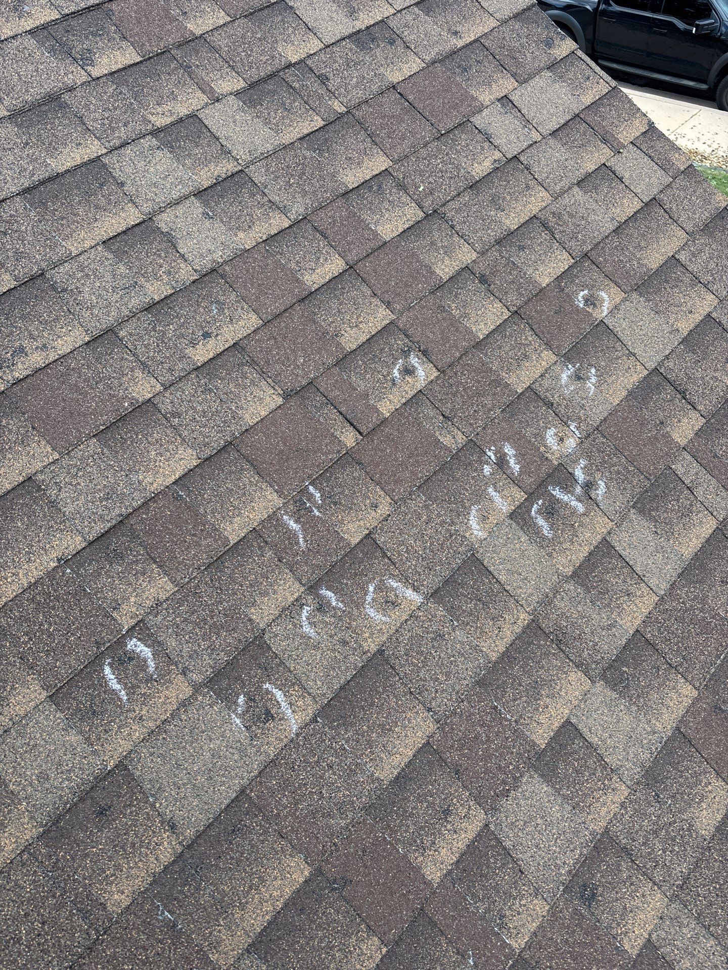 Hail impacts marked with chalk on asphalt shingles before replacement in Colorado Springs