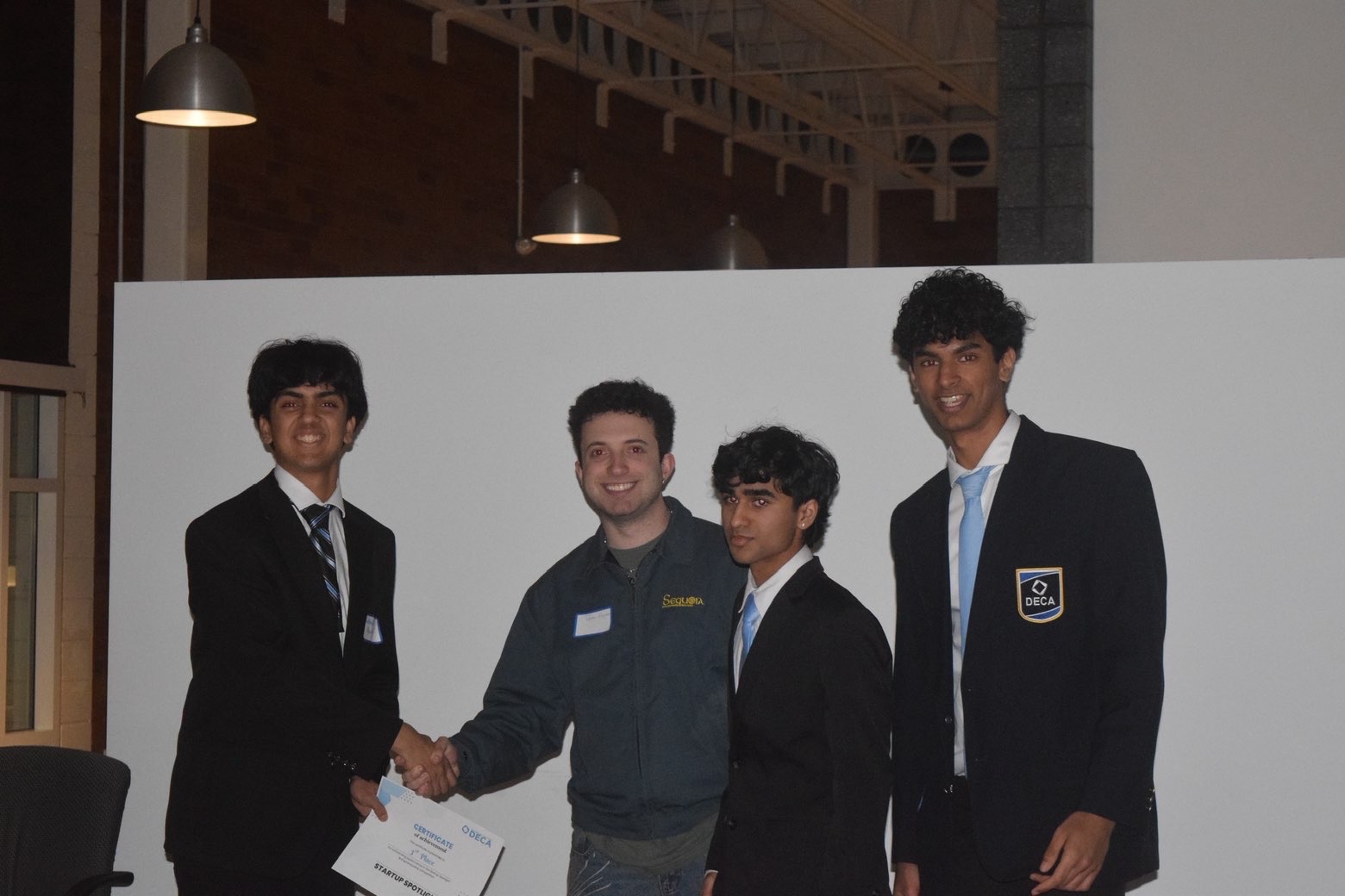 Students shaking hands while receiving a third place certificate at Startup Spotlight