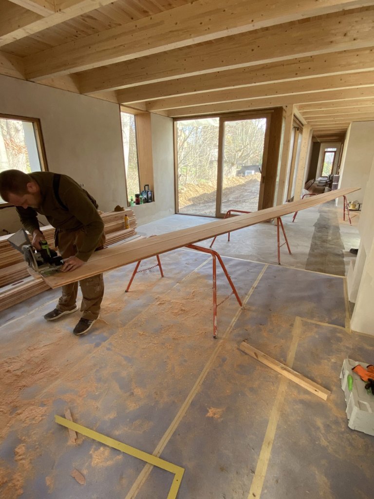 Tømrer tilsaver træbrædder til indvendig aptering i nyopført hus med synlige bjælker